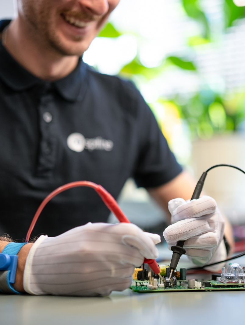 Mężczyzna w rękawiczkach testuje płytkę elektroniczną za pomocą miernika i sond pomiarowych.