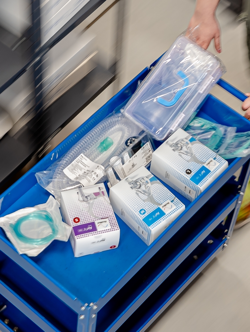 Wózek z zestawami medycznymi, maskami i rurkami prowadzony przez osobę w rękawiczce.