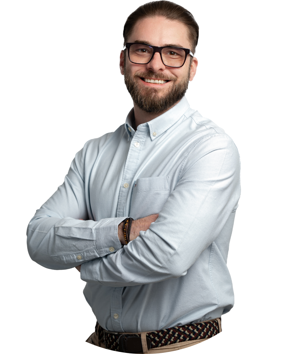 Mężczyzna w okularach i koszuli stoi z założonymi rękami, uśmiecha się do kamery.