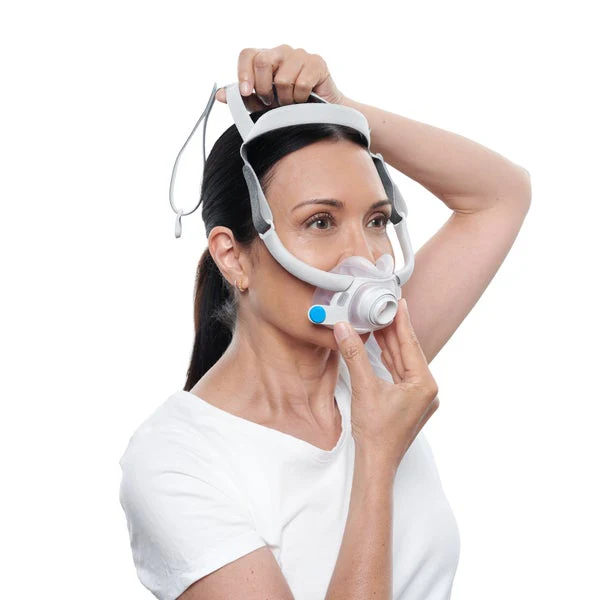 AirFitF40_Fitting_Female_11_720x Kobieta zakłada maskę CPAP na twarz, trzymając ją obiema rękami.